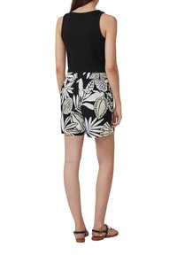 Haut sans manches noir associé à des shorts à motifs floraux noir et blanc. Les shorts comportent une taille élastique et des poches. Sandales visibles.
