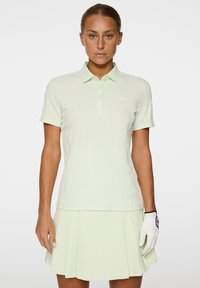 Hellgrünes Golf-Polo mit strukturiertem Muster und kurzen Ärmeln, ausgestattet mit einer Knopfleiste mit drei Knöpfen. Kombiniert mit einem passenden plissierten Rock.