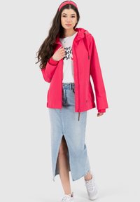 Rosa leichte Jacke mit Kapuze, getragen über einem weißen T-Shirt und einem Jeansrock mit Schlitz vorne. Kombiniert mit weißen Turnschuhen.