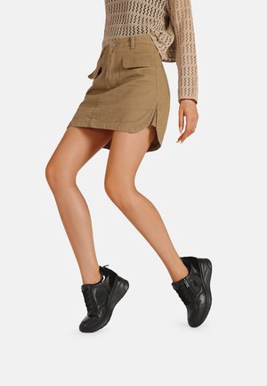 Gonna in denim khaki con spacchi laterali e due tasche, abbinata a sneakers nere con finitura texture e design con lacci.