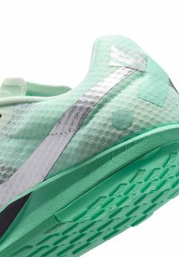 Chaussure de sport vert clair avec dessus en mesh texturé, accents argentés et semelle en caoutchouc présentant un motif antidérapant.