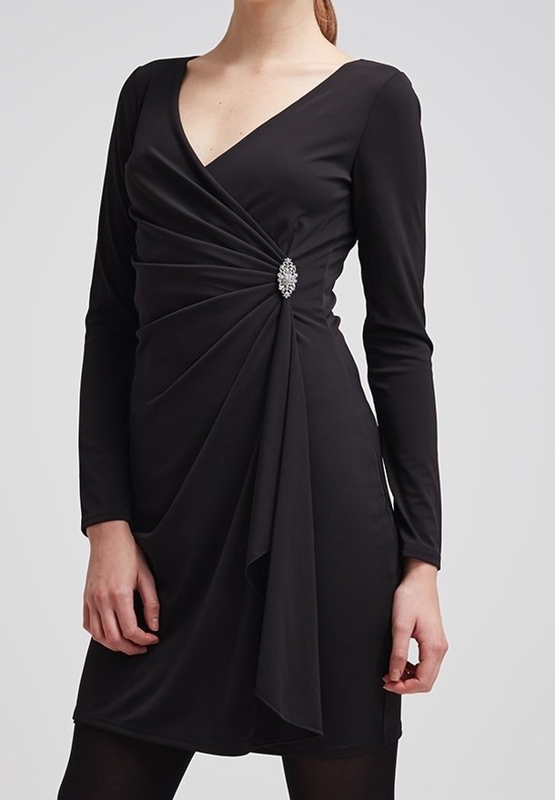 Robe noire à manches longues avec un col en V prononcé, présentant des détails froncés et une broche argentée à la taille. Tissu lisse et extensible.
