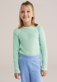 Mentazöld, hosszú ujjú, texturált felső válldíszítéssel, virágos hímzett részlettel, világoskék bordázott nadrággal párosítva.