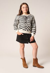 Zebra-patroontrui in crème en zwart, gecombineerd met een zwarte suède rok met knopen. Bruine suède enkellaarsjes maken de outfit compleet.