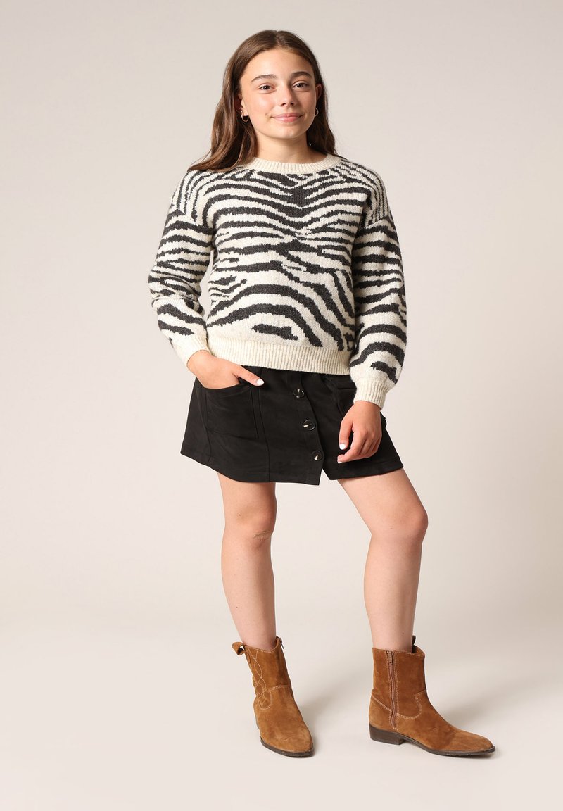 Zebra-patroontrui in crème en zwart, gecombineerd met een zwarte suède rok met knopen. Bruine suède enkellaarsjes maken de outfit compleet.