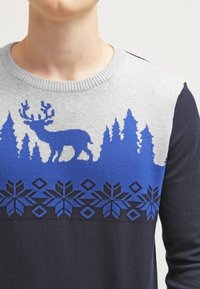 Szary i granatowy sweter z niebieską sylwetką jelenia, sosnowymi drzewami oraz geometrycznymi wzorami płatków śniegu na klatce piersiowej i ramionach.