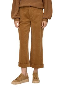 Bruine corduroy, wijde broekspijpen met opgerolde mouwen, gecombineerd met tan-kleurige veterschoenen, gepresenteerd op een onopvallende achtergrond.