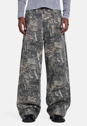 Pantalones de pierna ancha con un patrón abstracto en negro, gris y beige, combinados con zapatos negros y una camisa gris de manga larga.