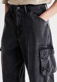 Svarta jeans cargo byxor med avslappnad passform, som har sidofickor, knappstängning och synlig sömnad. Strukturerad tyg med lätt blekning.