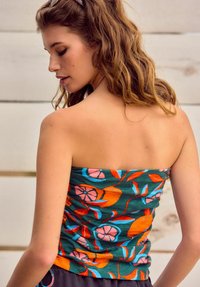 Haut sans bretelles avec un motif floral coloré comprenant des nuances d'orange, de rose et de bleu sur un fond vert foncé, texture froncée et coupe slim.