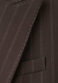 Tela marrón con rayas blancas finas, con solapa con muesca y un bolsillo en el pecho, que presenta un tejido texturizado y detalles de diseño a medida.