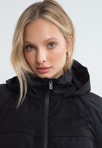 Black hooded jacket featuring a zippered front, smooth texture, and subtle seams. Lightweight design ideal for outdoor activities.