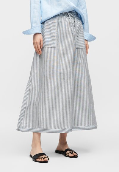 Person som har på seg en lyseblå skjorte og et langt grått og hvitt skjørt med vertikale striper og store fremre lommer, kombinert med svarte flipp-flopper.