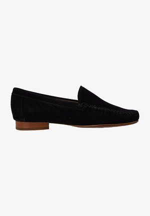 Mocassins en suède noir avec une semelle en caoutchouc brun plat, ornés de couture décorative et d'un style sans lacets. Texture lisse, design minimaliste.