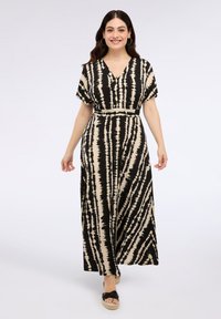 Vestido maxi en un patrón de tie-dye en negro y crema, con escote en V, mangas cortas y cintura ajustada, combinado con zapatos espadrilles planos.