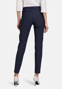 Marina skräddarsydda byxor med en slät textur, figursydd siluett och två bakfickor, tillsammans med beige högklackade skor.