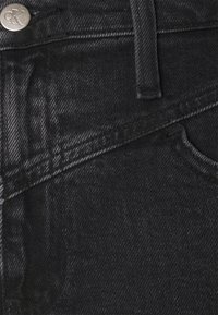 Black denim jeans featuring a smooth texture, topstitching detail, and CK branding on the metal button. Close-up view emphasizes fabric weave.