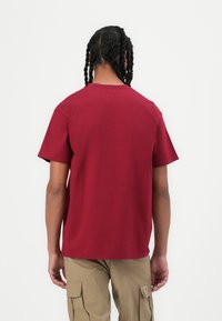 Maroon cotton t-shirt featuring a crew neck and short sleeves. The back is plain, with minimal seams and a relaxed fit.