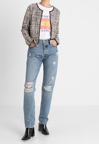 Stylowa tweedowa kurtka z czarnymi wykończeniami na koszulce z grafiką; zniszczone niebieskie dżinsy z przetarciami; czarne lakierowane botki za kostkę.