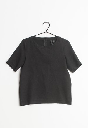Black short-sleeve top made of textured fabric, featuring a round neckline and a back zipper. Slightly boxy silhouette with loose fit.