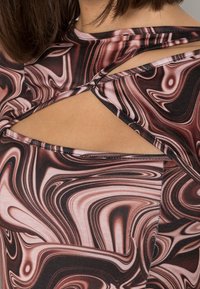 Istuutettu toppi pehmeästä kankaasta, jossa on musta ja pinkki pyörivä kuvio. Avonainen takamalli ristikkäisillä yksityiskohdilla parantaa hengittävyyttä.