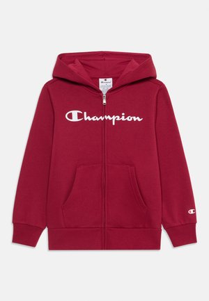 Hoodie rouge zippé avec un grand logo "Champion" blanc sur le devant, poches kangourou et poignets côtelés. Texture de tissu douce.