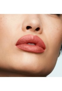 Gros plan sur des lèvres pleines recouvertes d'un rouge à lèvres mat pêche-rose, mettant en valeur une texture lisse et une forme définie sur une peau claire.