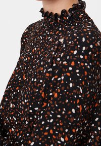 Blusa nera con motivo a macchie arancioni, bianche e marroni. Presenta un colletto frangiato, un tessuto texturizzato e una vestibilità rilassata.