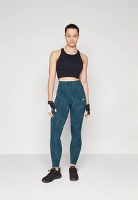 Črni športni kratki top, tajmasto zelene pajkice s vzorcem, črni športni čevlji, rokavice brez prstov, gladka tekstura, tesno prilegajoč dizajn.