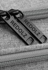 Twee zwarte ritstrekkers met het label "REDOLZ" op een gestructureerde grijze stofoppervlak met een zichtbare rits.