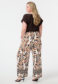Haut marron à manches courtes associé à un pantalon large avec un motif de feuilles dans des tons de marron, orange et crème, avec une bordure noire à l'ourlet.