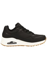 Chaussures de sport noires avec une tige lisse, des accents en mesh et un coussin d'air visible. Elles disposent de lacets noirs, d'une semelle blanche et d'une semelle extérieure en caoutchouc naturel.