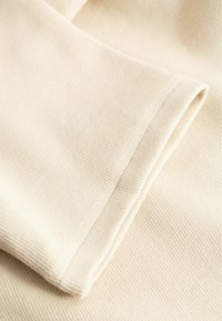 Gros plan sur un tissu côtelé de couleur crème plié pour montrer un ourlet soigneusement cousu sur une manche ou un poignet.