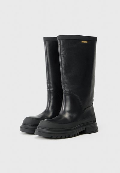 Höga svarta läderstövlar med tjocka gummisulor och en liten gyllene "Missoni"-logotyp nära överkanten av varje stövel.