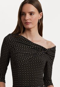 Svart av-shoulder topp med samlet tekstur og liten beige rutemønster, med tre kvarte ermer og en tettsittende design.
