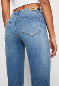 Ljust blårandiga jeans med slim fit, med bakfickor, subtila sömnadsdetaljer, och en brun etikett på midjebandet.