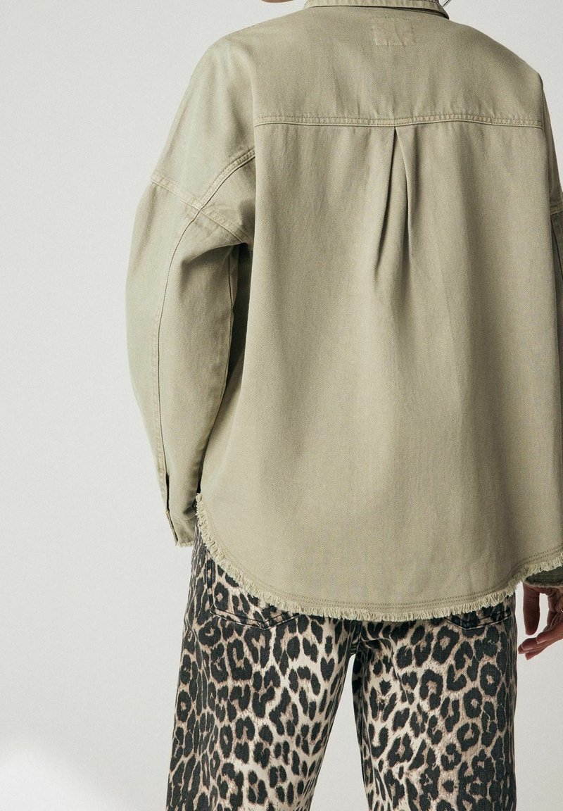 Chemise beige à manches longues avec pli et ourlet effiloché associée à un pantalon taille haute imprimé léopard, vue de dos.