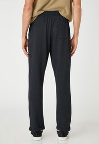 Donkergrijze, gestructureerde joggingbroek met een elastische tailleband en een achterzak. Omgeslagen broekspijpen en gedragen met zwarte sneakers.