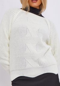 Maglione a trecce crema con una vestibilità ampia, dotato di polsini e orlo a coste, motivo testurizzato e un tessuto morbido e leggero.