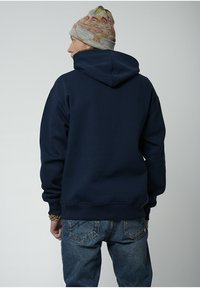 Sudadera con capucha azul marino hecha de un tejido suave, presenta un bolsillo tipo canguro y puños de canalé, combinada con vaqueros de un azul desgastado y un gorro de lana con estampado.