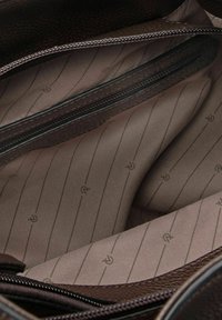 Intérieur texturé marron d'un sac avec une poche zippée et une doublure en tissu lisse avec des motifs rayés subtils.