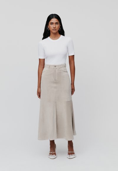 Beige Wildleder-Midirock mit ausgestelltem Saum, Frontknopf- und Reißverschluss, kombiniert mit einem enganliegenden weißen T-Shirt mit kurzen Ärmeln.