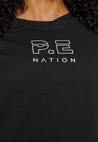 Black t-shirt made of cotton featuring a white graphic print with the text "P.E NATION" prominently displayed on the front.
