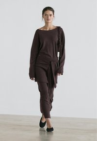 Maroon knitted two-piece outfit featuring a long-sleeve top and matching pants with a tie detail at the waist, accompanied by black flats.