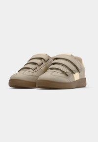 Paire de chaussures décontractées beiges avec trois larges bandes Velcro et semelles en caoutchouc marron sur un fond clair uni.