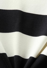 Gros plan d'un tissu tricoté avec de larges rayures horizontales noires et blanches montrant la texture et les plis.