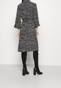 Svart och vit mönstrad klänning med långa ärmar, rynkade manschetter och resårmidja, som bärs med svarta knähöga stövlar.