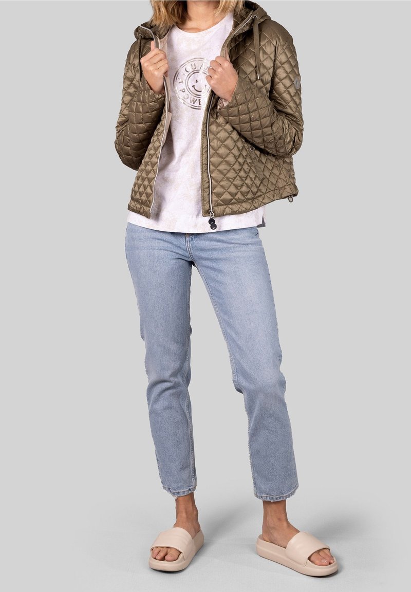 Quilted olivengrøn jakke med hætte, lys grå grafisk t-shirt, lyseblå jeans og beige slidesandaler. Glatte teksturer og afslappet pasform.