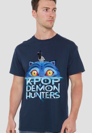 Marineblaues Baumwoll-T-Shirt mit einem Motiv einer blauen Katze mit großen gelben Augen und einem schwarzen Hut sowie dem Schriftzug „K-POP DEMON HUNTERS“ in fetten Buchstaben.