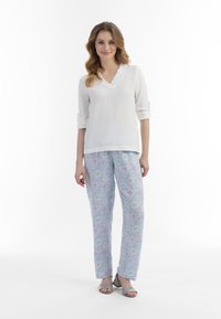 Hvid, langærmet top med V-hals og opkrøllede ærmer. Lyseblå bukser med blomsterprint i pink og mint nuancer. Grå sandaler med åben tå.